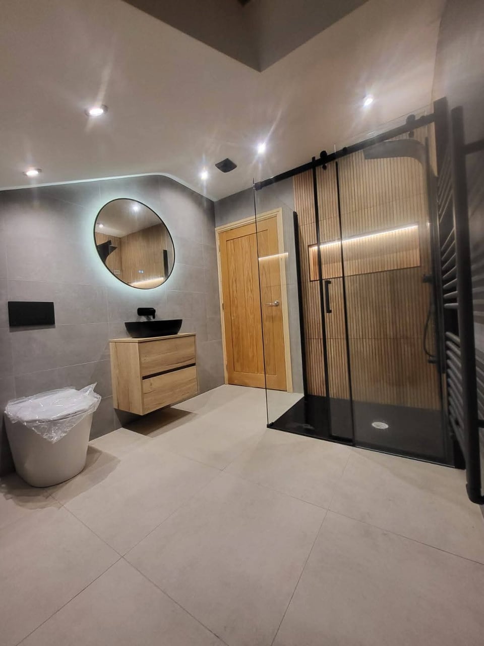 Modern grey bathroom with a black-framed shower, floating vanity unit and illuminated round mirror