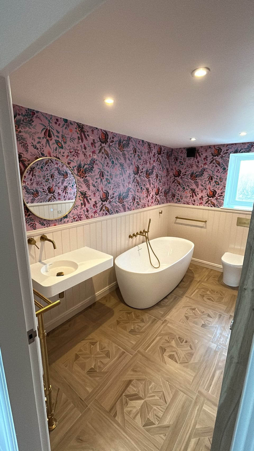 Finished bathroom with a freestanding bath, wall-mounted basin, brass fittings and floral wallpaper