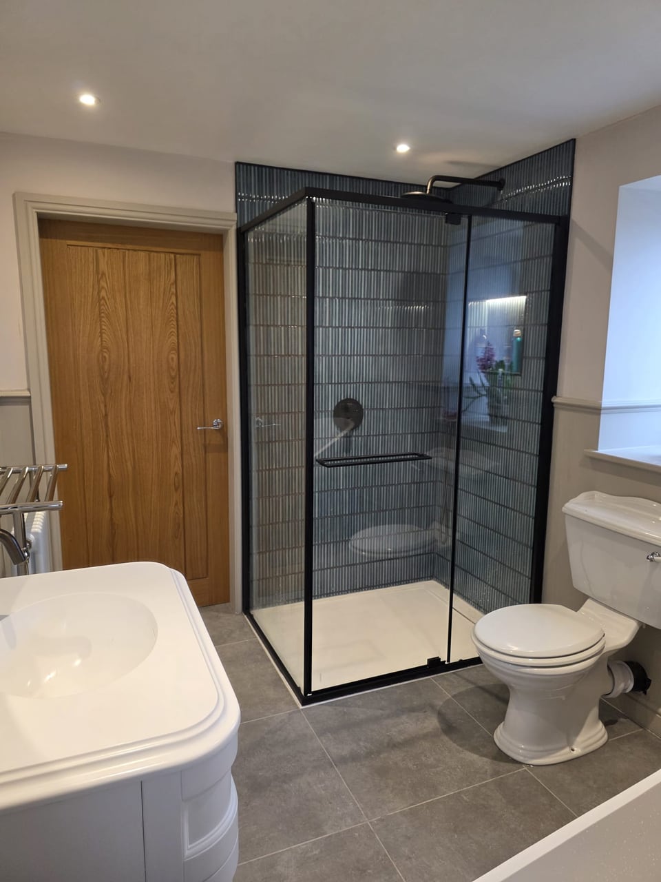 Black-framed ribbed-glass shower, white vanity unit and toilet in a finished bathroom