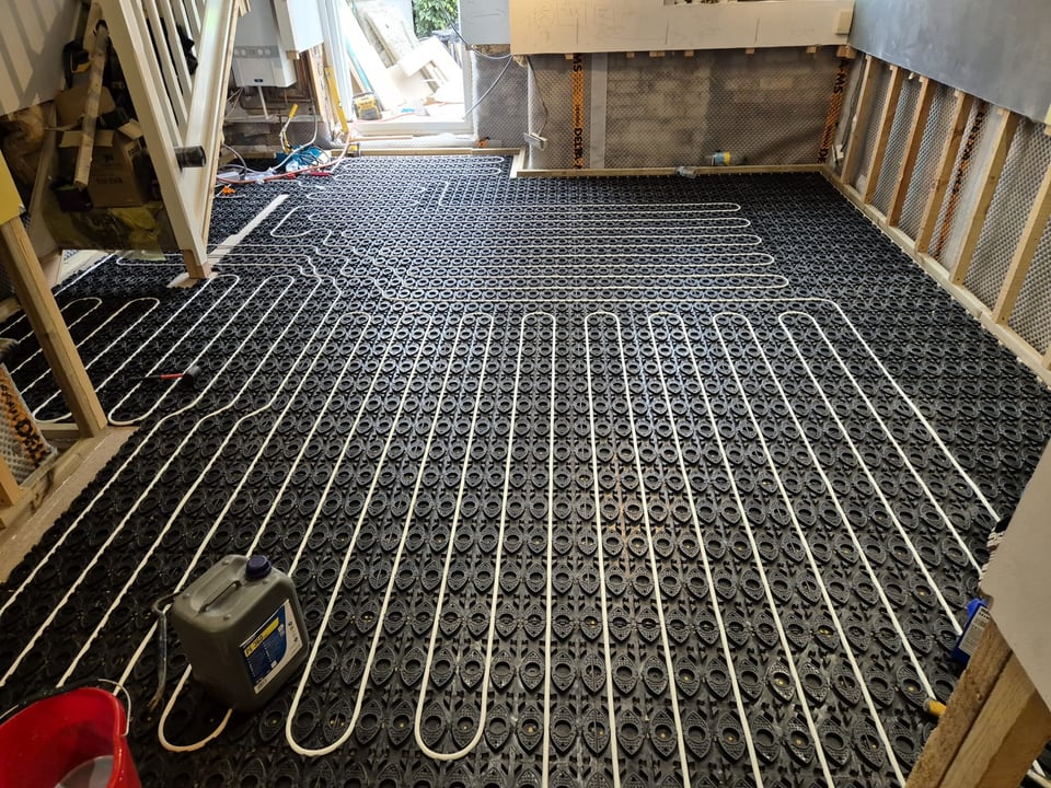 White underfloor heating pipework laid across black floor panels during installation